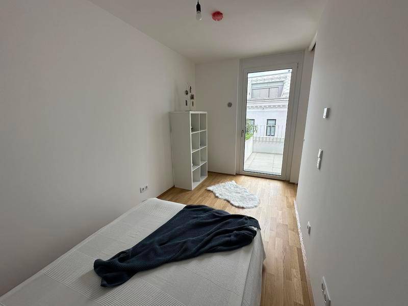 Helles Schlafzimmer mit Holzboden, minimalistischer Einrichtung und Balkonzugang.