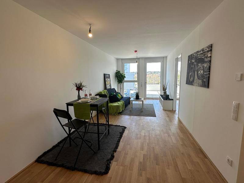 Heller Wohn- und Essbereich mit Holzfußboden und Zugang zum Balkon.