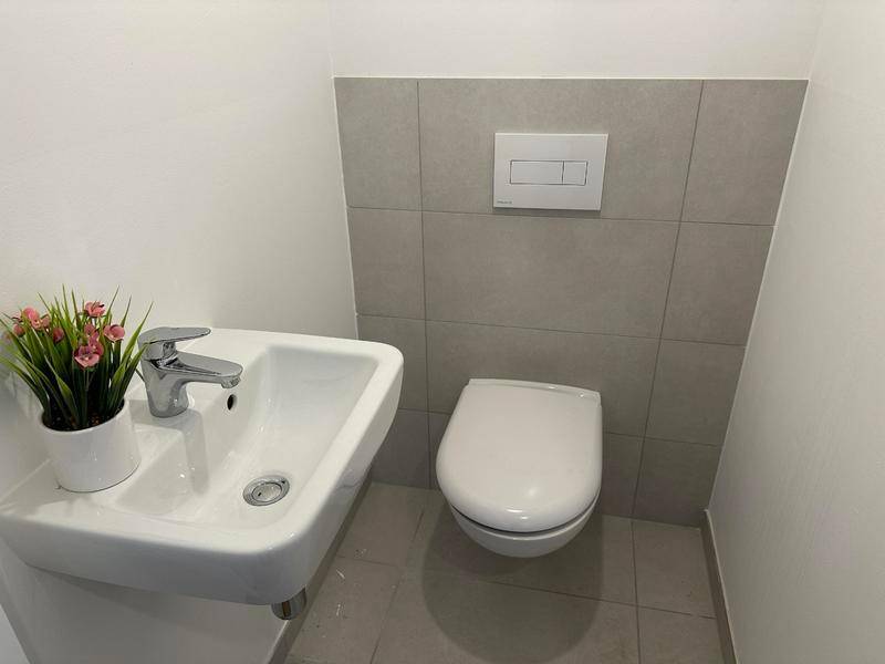 Gäste-WC mit Wand-WC, kleinem Waschbecken und modernen Fliesen.