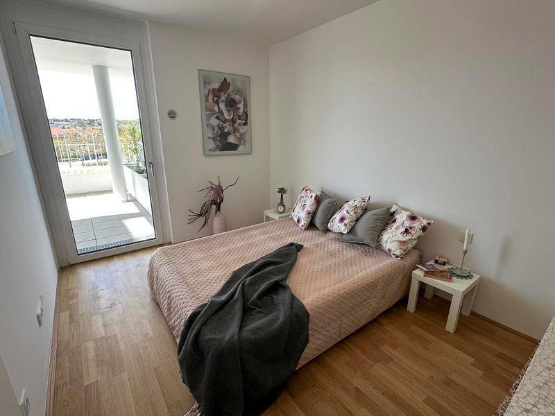 Schlafzimmer mit Holzboden, Doppelbett und großem Fenster mit Balkonzugang.