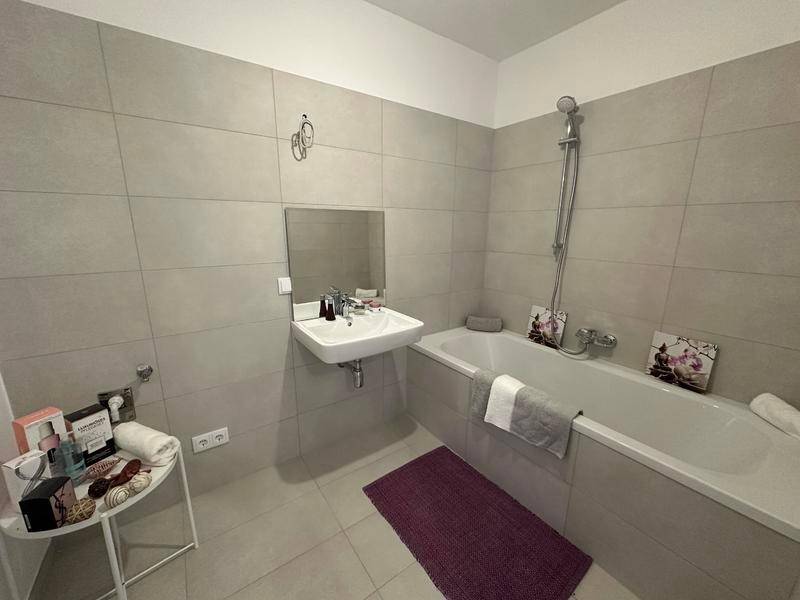 Modernes Badezimmer mit hellgrauen Fliesen, Badewanne und Einzelwaschbecken.