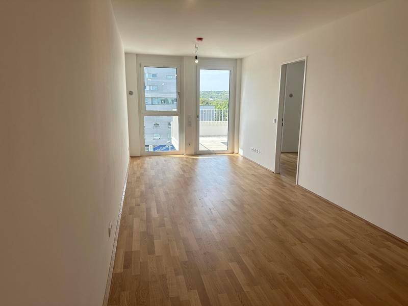 Heller, leerer Raum mit Holzboden und Zugang zu einem Balkon oder einer Terrasse.