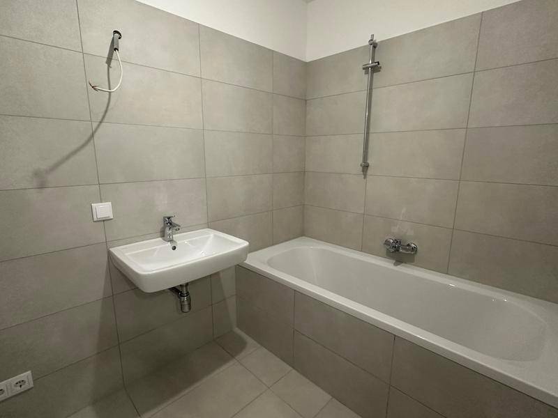 Modernes Badezimmer mit hellgrauen Fliesen, Waschbecken und Badewanne mit Duschfunktion.