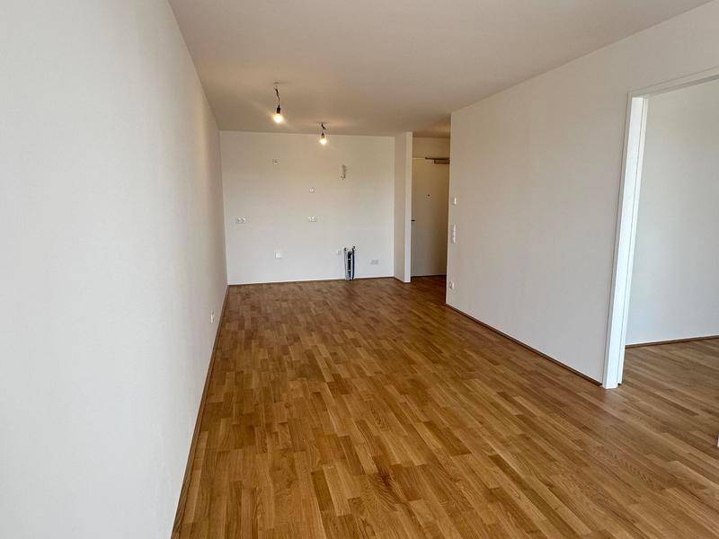 Leerer Raum mit Holzboden und weißen Wänden, vorbereitet für die Installation einer Küche oder als Wohnbereich.