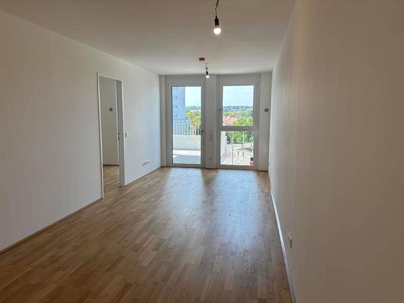 Heller Wohnraum mit Holzboden und Zugang zu einem Balkon, ideal für individuelle Gestaltung.