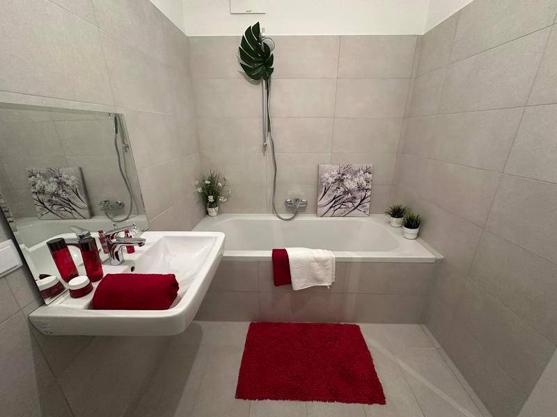 Funktionales Badezimmer mit Badewanne, Waschbecken und hellen Fliesen an Wänden und Boden.