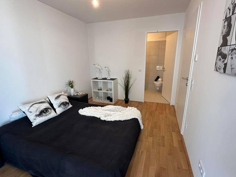 Helles Schlafzimmer mit Holzboden und Blick auf das angrenzende Badezimmer.