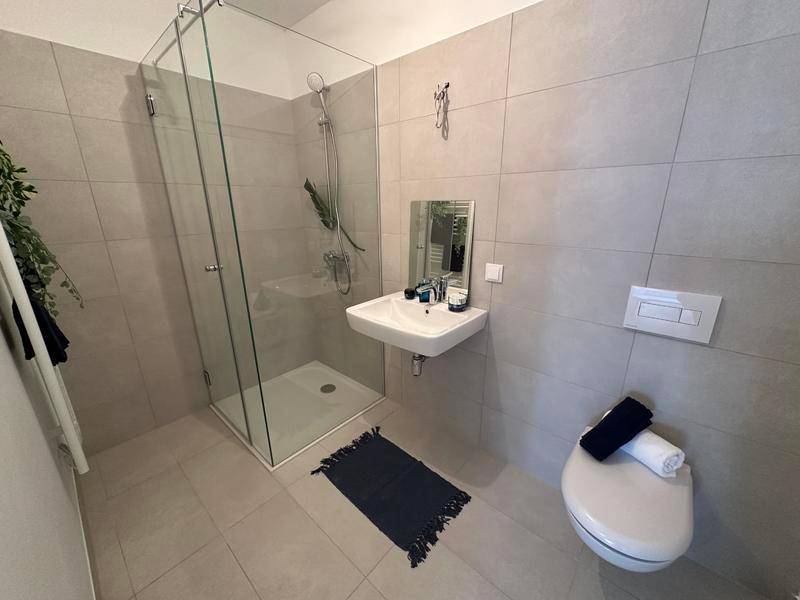 Modernes Badezimmer mit ebenerdiger Dusche, Wand-WC und hellem Fliesenboden.