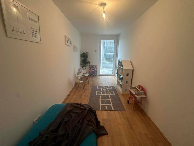 Kinderfreundliches Zimmer mit Holzboden und Zugang zu einem Außenbereich, ideal zum Spielen.