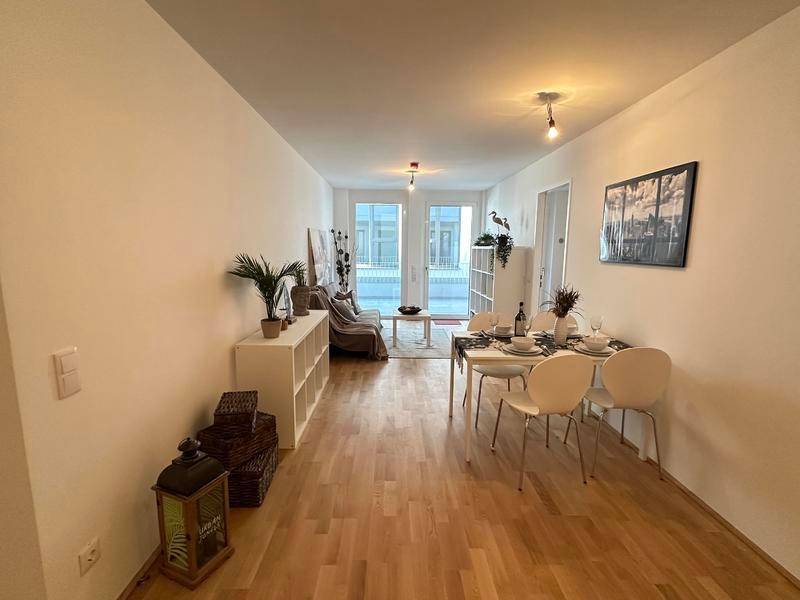 Heller Wohn- und Essbereich mit Holzparkett und Zugang zum Balkon, modern eingerichtet.