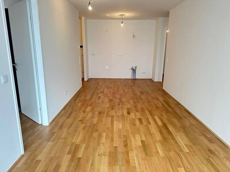 Leerer Raum mit Parkettboden und Anschlüssen für eine zukünftige Küche oder Wohnbereich.