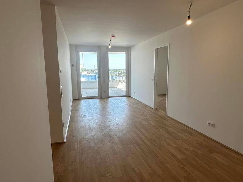 Heller, leerer Raum mit Holzboden und Zugang zu einer großen Terrasse.