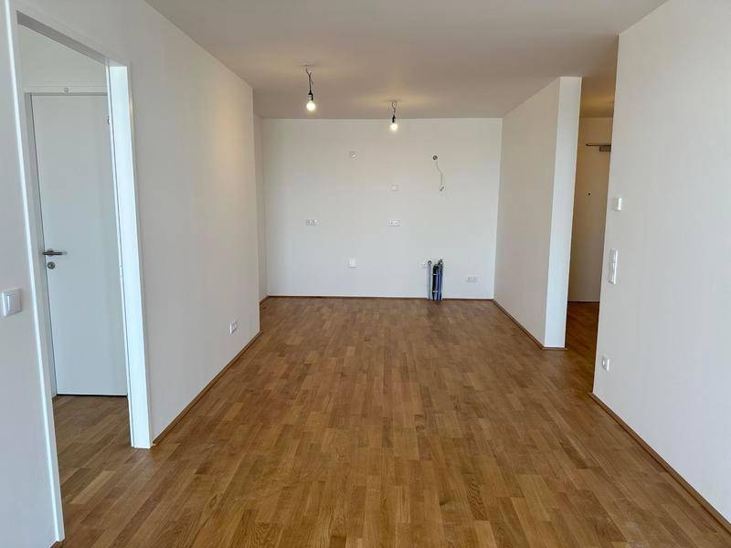 Geräumiger, unmöblierter Wohnbereich mit hellem Holzboden und weißen Wänden.