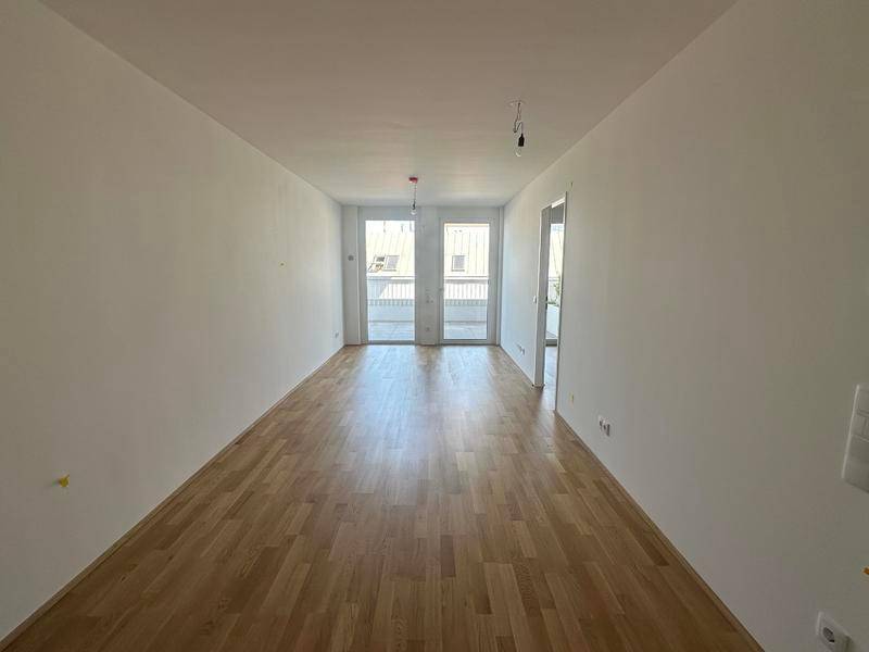 Heller, leerer Wohnraum mit Parkettboden und Zugang zu einem Balkon.