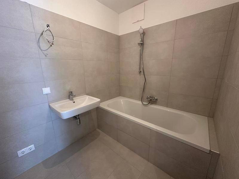 Badezimmer mit Badewanne, Waschbecken und grauen Fliesen an Wänden und Boden.