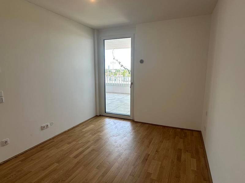 Helles Schlafzimmer mit Holzboden und Zugang zu einem Außenbereich, bereit zur Einrichtung.