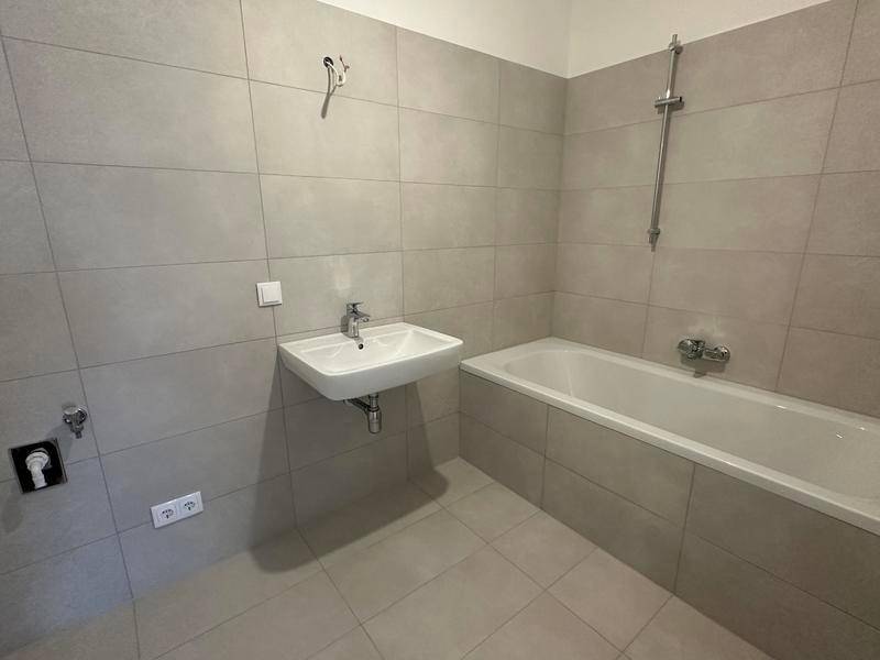 Modernes Badezimmer mit Badewanne, Waschbecken und grauen Wand- und Bodenfliesen.