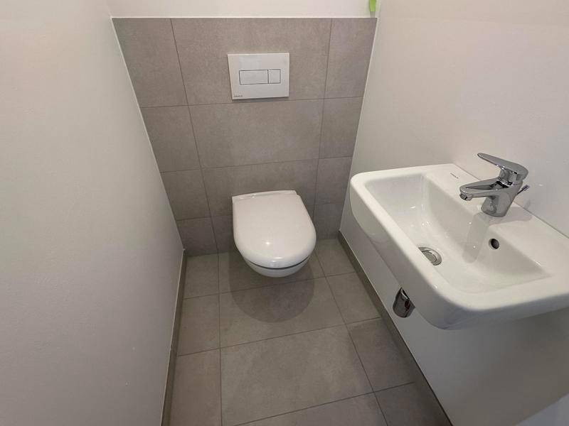 Kleines Gäste-WC mit Wand-WC, Handwaschbecken und grauen Fliesen.
