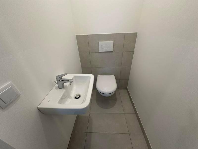 Kleines Gäste-WC mit Wand-WC, Waschbecken und grauen Wand- und Bodenfliesen.