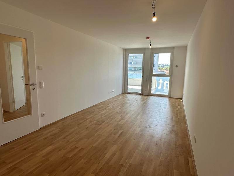 Heller, leerer Raum mit Holzboden und Zugang zu einem Balkon oder einer Terrasse.