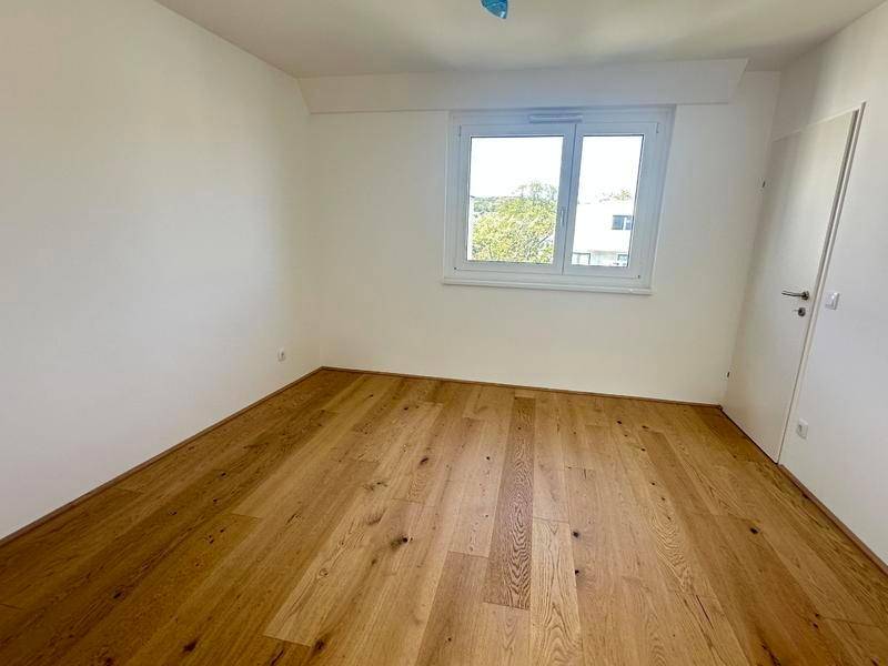 Geräumiges Schlafzimmer mit Holzboden und Fenster, bereit zur individuellen Gestaltung.