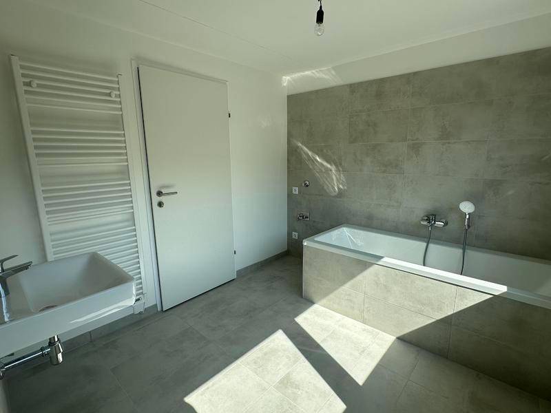 Helles Badezimmer mit Badewanne, Handtuchheizkörper und modernen grauen Fliesen.