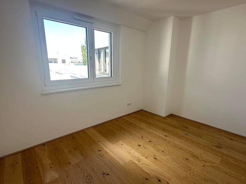 Leeres Schlafzimmer mit Holzboden und großem Fenster für viel Tageslicht.