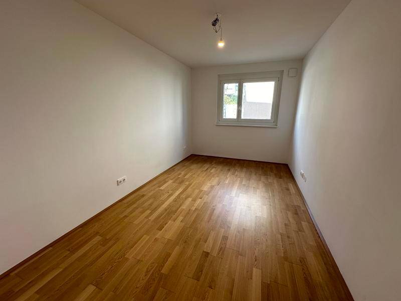 Leeres Zimmer mit Holzfußboden und Fenster, das viel Tageslicht hereinlässt.