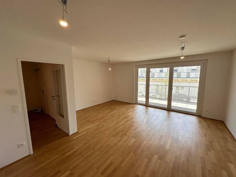 Leeres Wohnzimmer mit Parkettboden, viel Tageslicht und Zugang zu weiteren Räumen.
