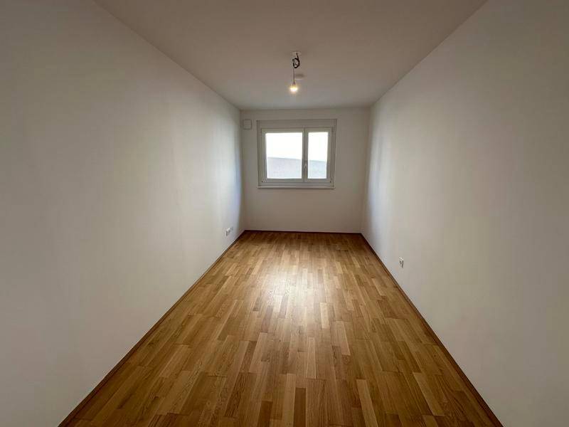 Helles Zimmer mit Holzfußboden und Fenster, bereit zur individuellen Gestaltung.
