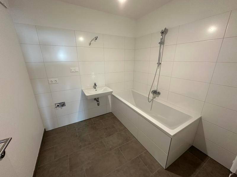 Modernes Badezimmer mit weißen Fliesen, Badewanne mit Duschfunktion und kleinem Waschbecken.
