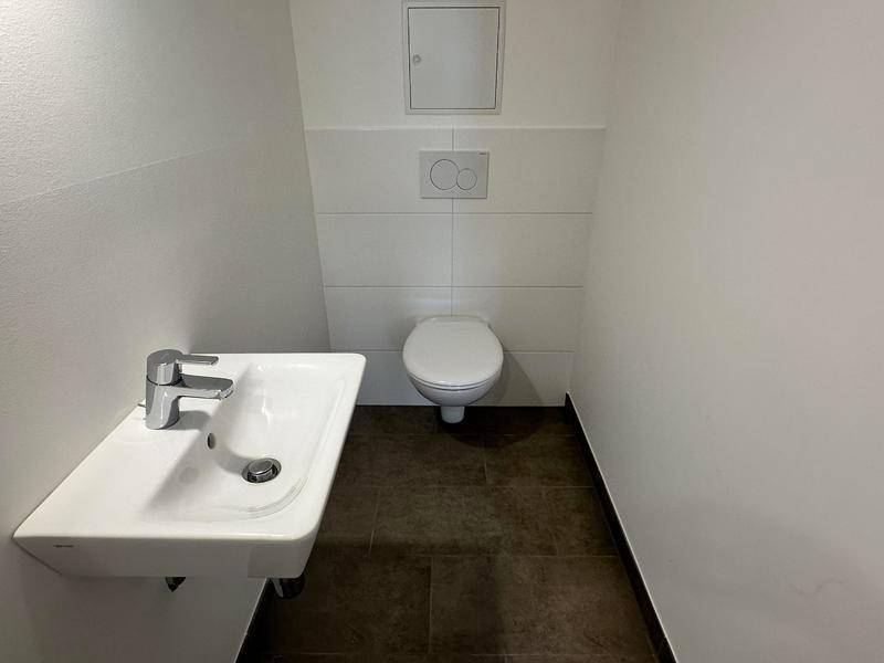 Gäste-WC mit wandhängender Toilette und kleinem Waschbecken, modern gefliest.
