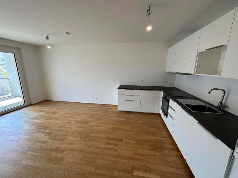 Offener Wohnbereich mit integrierter moderner Küche, Holzfußboden und Balkonzugang.