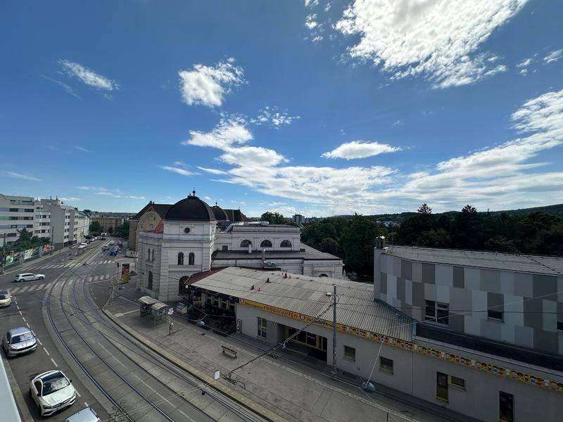 Panoramablick über eine Stadtstraße mit Straßenbahnschienen und grünen Hügeln im Hintergrund.
