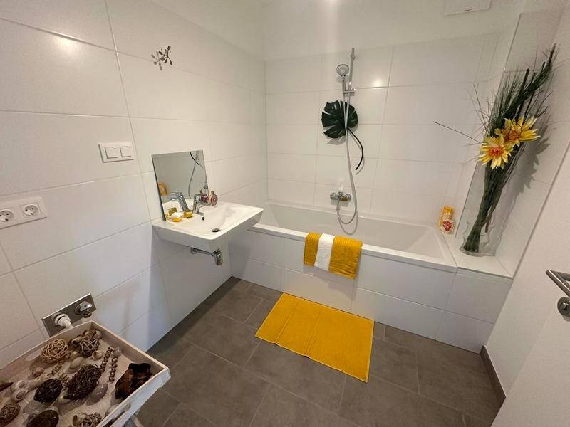 Modernes Badezimmer mit weißen Fliesen, Badewanne mit Duschfunktion und Einzelwaschbecken.