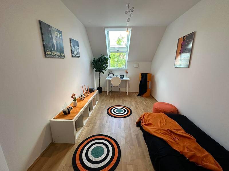 Helles Zimmer mit Dachschräge, Holzboden und Dachfenster, eingerichtet als Kinder- oder Gästezimmer.