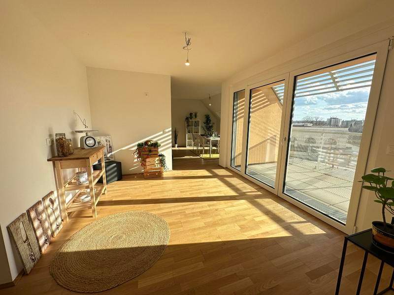 Helles, unmöbliertes Wohnzimmer mit Holzboden und großen Schiebetüren zum Balkon.