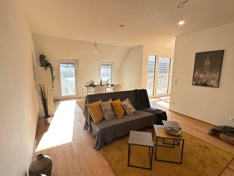 Gemütlicher Wohn-Essbereich mit Holzboden, Sofa und Esstisch unter einer Dachschräge.