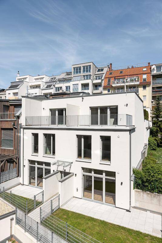 Moderne weiße Wohngebäude mit Terrassen und Grünflächen unter blauem Himmel.