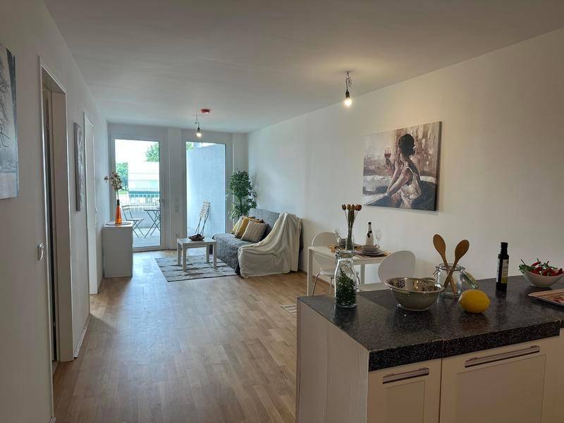 Heller offener Wohnbereich mit integrierter Küchenzeile, Holzboden und Zugang zum Balkon.