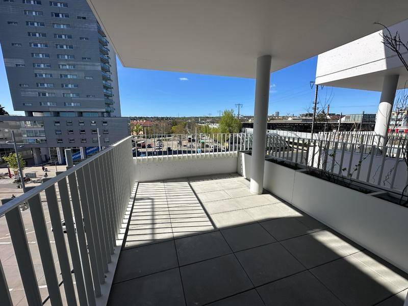 Geräumiger Balkon mit Fliesenboden und Blick auf die Stadt und umliegende Gebäude unter blauem Himmel.