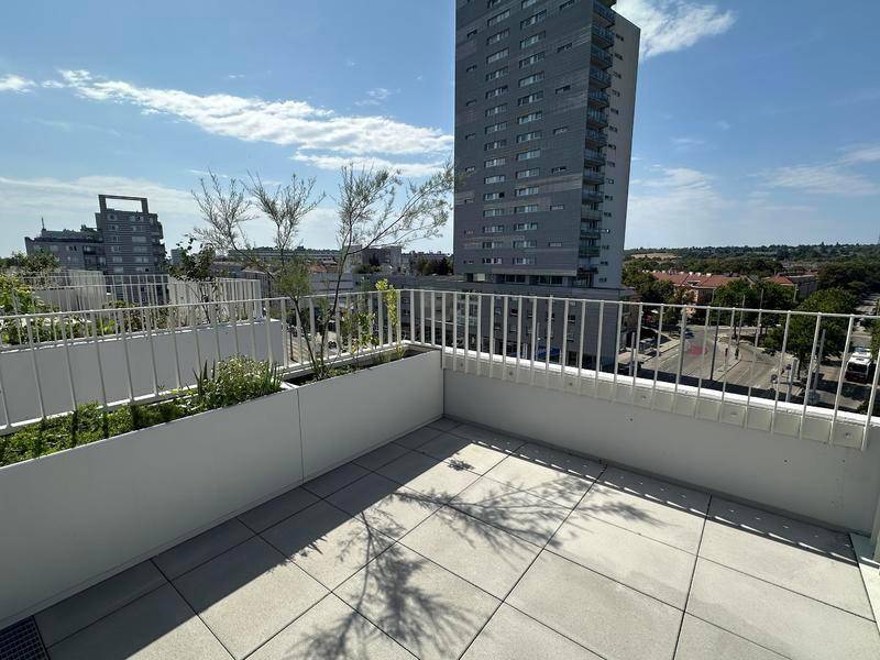 Geräumige Dachterrasse mit Fliesenboden und Blick auf die Stadt und umliegende Gebäude.