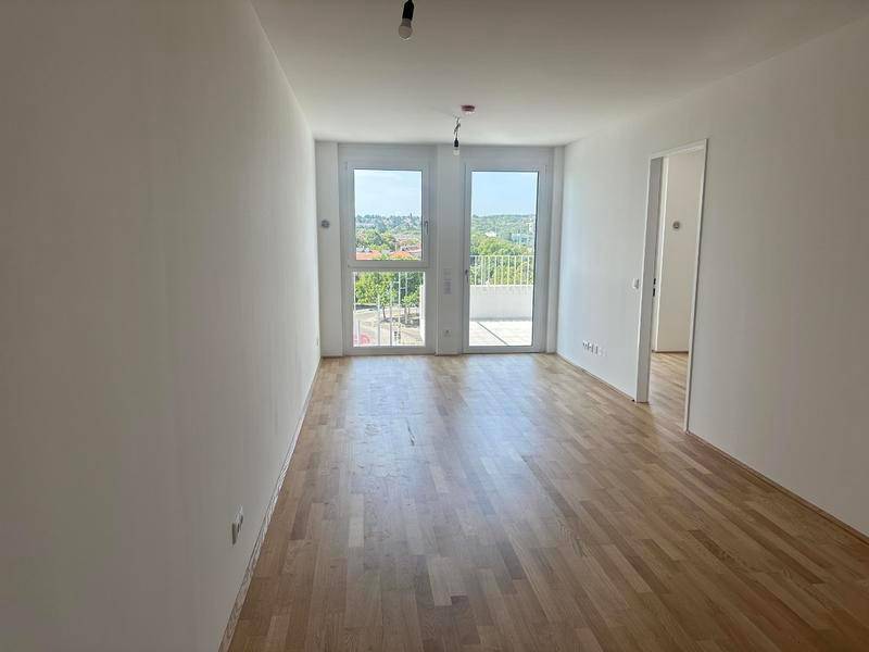 Heller, leerer Wohnraum mit Holzboden und Zugang zu einem Balkon mit Stadtblick.