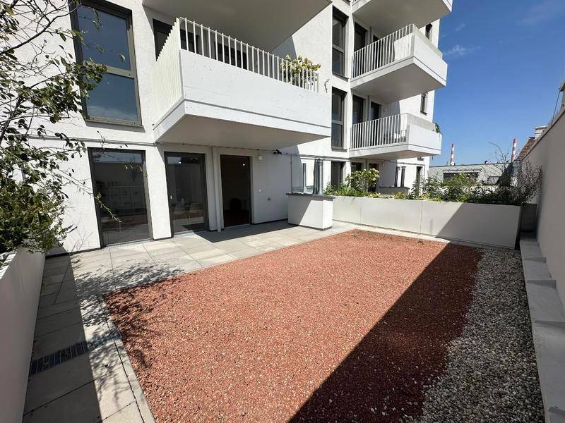 Große, sonnige Terrasse mit Kiesfläche und Zugang zu modernen Wohnräumen im Erdgeschoss.