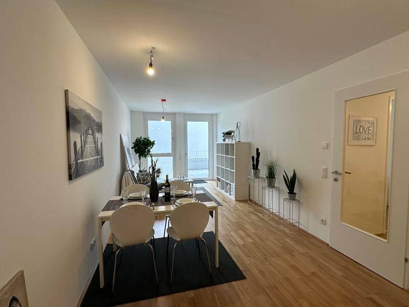 Heller Wohn- und Essbereich mit Holzboden, modernem Esstisch und Zugang zum Balkon.