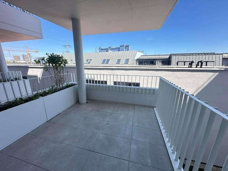 Heller Balkon mit Fliesenboden, weißem Geländer und Blick auf die umliegenden Gebäude.