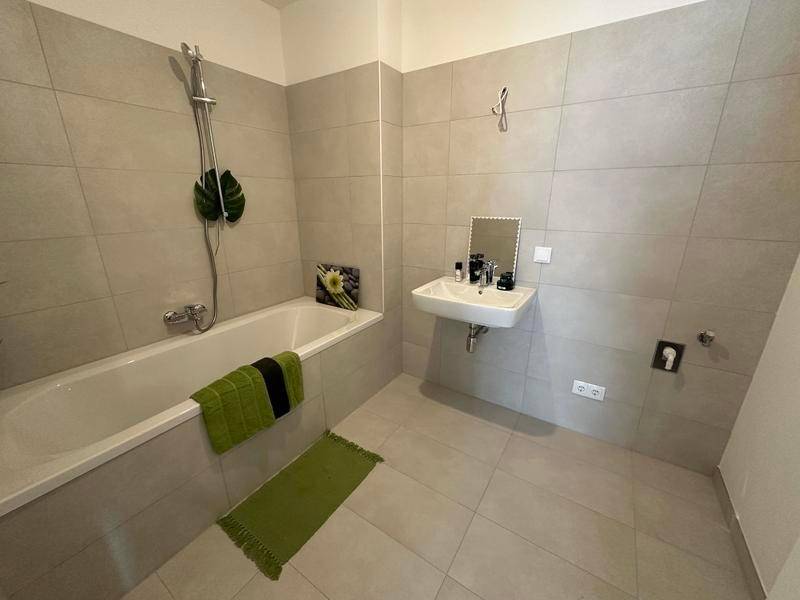 Modernes Badezimmer mit Badewanne, Waschbecken und hellgrauen Fliesen an Wänden und Boden.