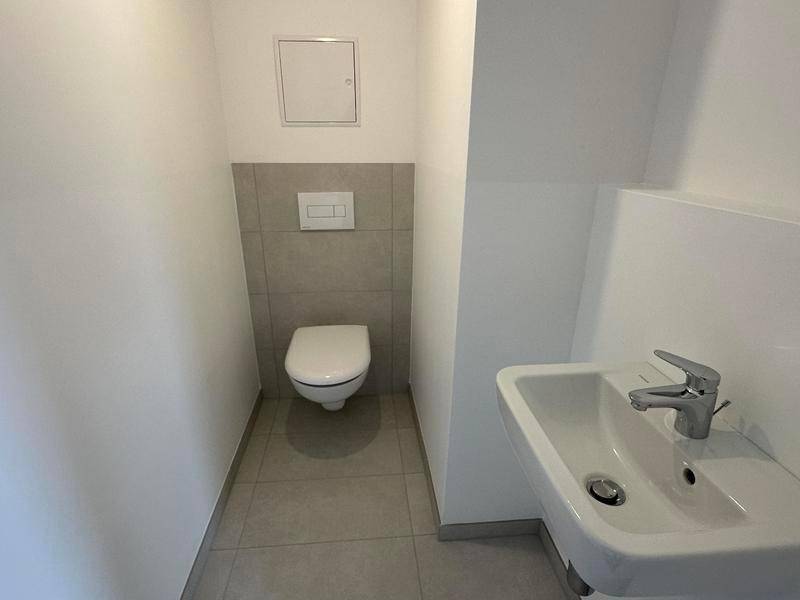 Modernes Gäste-WC mit wandhängender Toilette und kleinem Waschbecken in neutralen Farben.