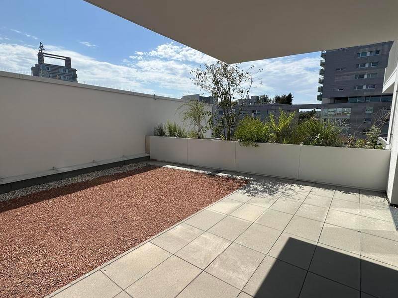 Geräumige Terrasse mit Fliesenboden, Kiesbereich und begrünten Pflanzbeeten unter blauem Himmel.