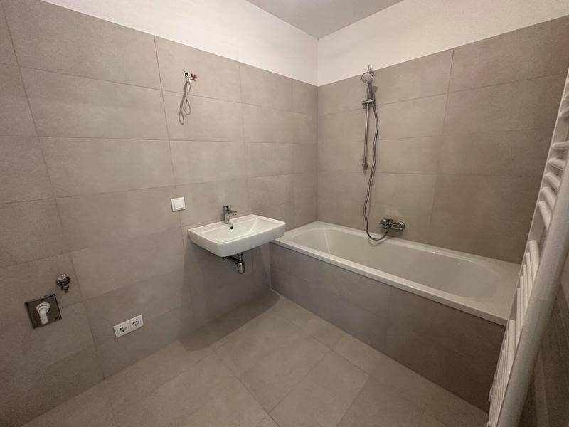 Modernes Badezimmer mit Badewanne, Waschbecken und beheiztem Handtuchhalter in hellen Fliesen.